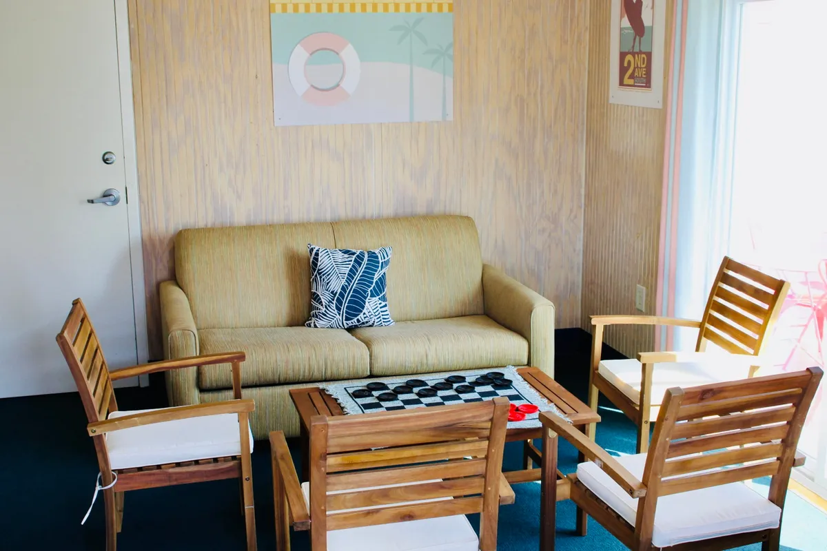 An open-plan living area with a comfortable sofa, a checkers board set out, wall art, and wooden chairs, inviting guests to unwind, play games, or socialize in a casual and friendly atmosphere.