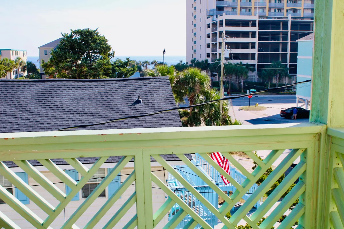 This tranquil view showcases a scenic balcony overlooking the ocean, dotted with palm trees, an American flag, and modern buildings. The scene evokes moments of relaxation and connection to the outdoors—ideal for spontaneous beach trips and sunset strolls.